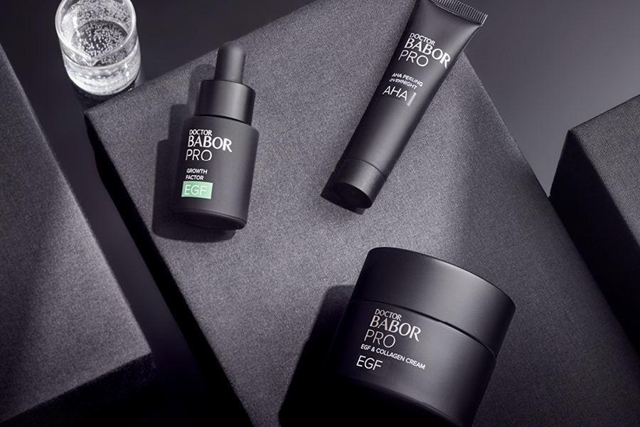Drei elegante Doctor BABOR PRO Produkte – Serum, Peeling und Creme – stilvoll auf grauen Boxen arrangiert.